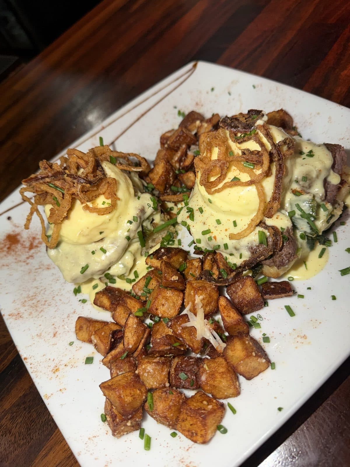 Steakhouse Benedict with tenderloin, Utica greens, two poached eggs, gorgonzola hollandaise and crispy onions over house breakfast potatoes