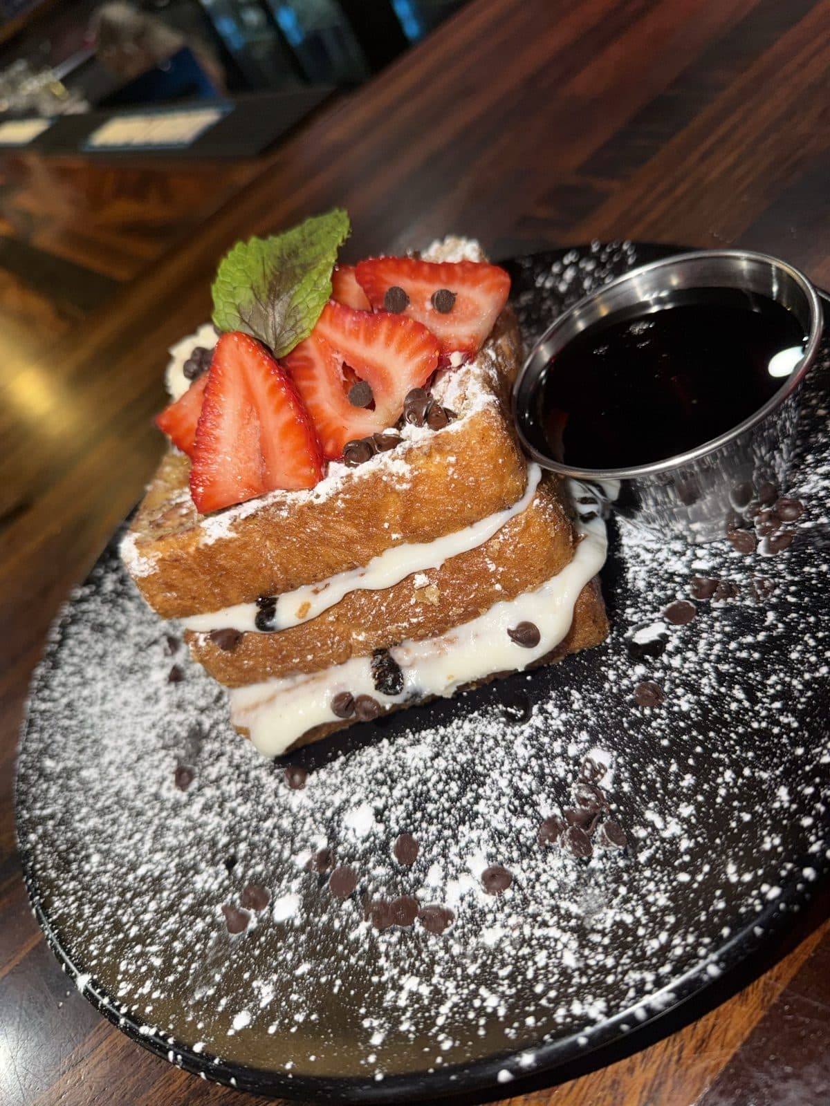 Cannoli Crunch French Toast stuffed with cannoli cream, topped with fresh strawberries, mini chocolate chips and powdered sugar